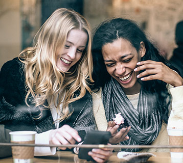 two young adult females laughing together while looking at their phone