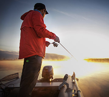 young adult male fishing on a boat at sunrise