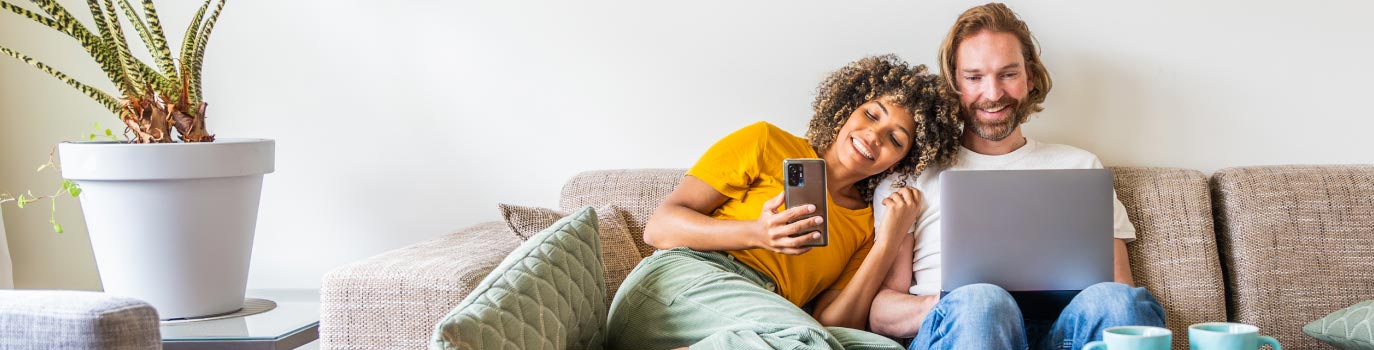 A young couple using laptop and smart phone sitting on the sofa at home